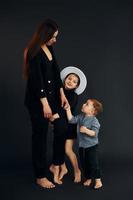 vrouw in zwart elegant kleren is met haar weinig zoon en dochter in de studio foto