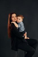 moeder in elegant zwart kleren is met haar weinig zoon in de studio foto