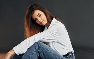 in wit overhemd en blauw jeans. jong mooi vrouw is poseren voor de camera in de studio foto