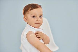 schattig weinig jongen zit na vaccin injectie binnenshuis in ziekenhuis foto