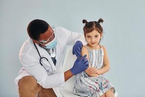 jong Afrikaanse Amerikaans dokter geven injectie naar weinig meisje Bij ziekenhuis foto