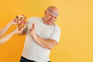 handen met hamburgers verleidt jongen. grappig te zwaar Mens in sportief hoofd stropdas is tegen geel achtergrond foto