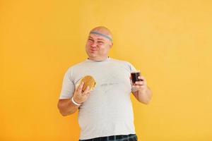 met snel voedsel. grappig te zwaar Mens in sportief hoofd stropdas is tegen geel achtergrond foto