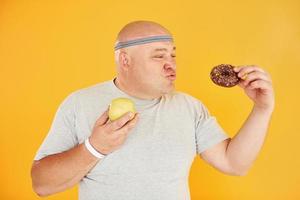 appel of koekje. grappig te zwaar Mens in sportief hoofd stropdas is tegen geel achtergrond foto