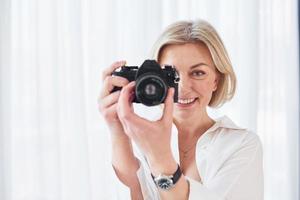 middelbare leeftijd vrouw in elegant kleren is Bij huis. fotograaf met camera foto