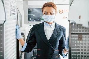 in masker. jong stewardess Aan de werk in de passagier vliegtuig foto