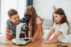 gebruik makend van microscoop. kinderen hebben pret in de huiselijk kamer Bij dag samen foto