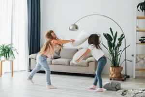 meisjes zijn spelen hoofdkussen strijd spel. kinderen hebben pret in de huiselijk kamer Bij dag samen foto