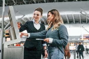 werknemer helpen naar gebruik terminal. jong vrouw toerist is in de luchthaven Bij dag foto