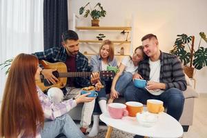 spelen akoestisch gitaar. groep van vrienden hebben partij binnenshuis samen foto