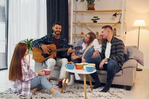 spelen akoestisch gitaar. groep van vrienden hebben partij binnenshuis samen foto