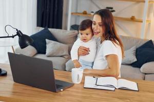 laptop is Aan de tafel. moeder met haar weinig dochter is Bij huis samen foto