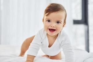 spelen Aan de bed. schattig weinig baby is binnenshuis in de huiselijk kamer foto