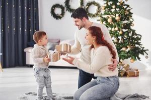 geven Cadeau naar de jongen. vader en moeder met zoon is Bij huis vieren nieuw jaar samen foto