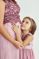 vrouw is zwanger. moeder in jurk staand met haar dochter in de studio met wit achtergrond foto