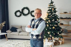 vieren nieuw jaar en staand in de buurt Kerstmis boom. senior Mens in mooi hoor kleren is Bij huis foto