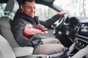 Mens zittend in de auto- en Holding weinig rood speelgoed- auto in hand- foto