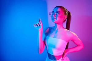 met kauwen gom. modieus jong vrouw staand in de studio met neon licht foto