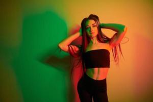 tegen muur. modieus jong vrouw staand in de studio met neon licht foto