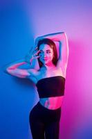 in zwart kleren. modieus jong vrouw staand in de studio met neon licht foto