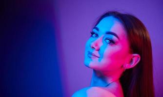 dichtbij omhoog visie. modieus jong vrouw staand in de studio met neon licht foto