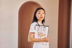 documenten in handen. jong echt Aziatisch vrouw staand binnenshuis foto