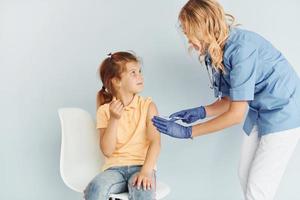 weinig meisje in geel shirt. dokter in uniform maken vaccinatie naar de geduldig foto