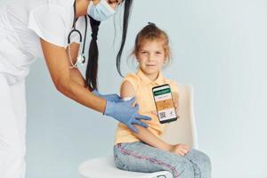 dokter in uniform maken vaccinatie naar de weinig meisje foto