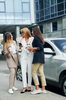 Dames in formeel slijtage is buitenshuis in de stad samen staand in de buurt zilver gekleurde auto foto