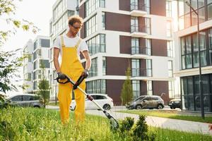 modern gebouwen. Mens besnoeiing de gras met gazon verhuizer buitenshuis in de werf foto