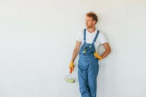 tegen wit muren. jong Mens werken in uniform Bij bouw Bij dag foto