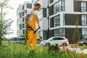 modern gebouwen. Mens besnoeiing de gras met gazon verhuizer buitenshuis in de werf foto