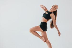 in de studio tegen wit achtergrond. jong vrouw in sportief kleren aan het doen gymnastiek binnenshuis foto