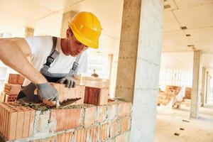 werken door gebruik makend van bakstenen. jong Mens in uniform Bij bouw Bij dag foto