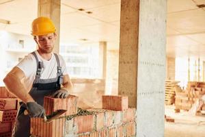 werken door gebruik makend van bakstenen. jong Mens in uniform Bij bouw Bij dag foto