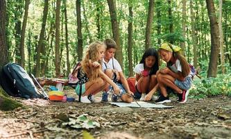 zittend Aan de grond. kinderen wandelen in de Woud met reizen uitrusting foto