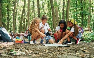 zittend Aan de grond. kinderen wandelen in de Woud met reizen uitrusting foto