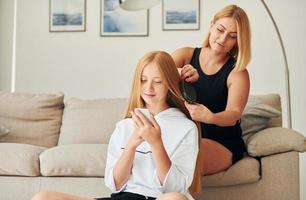 aan het doen kapsel. vrouw tiener met haar moeder is Bij huis Bij dag foto