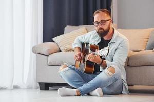 creatief bezigheid. Mens in gewoontjes kleren en met akoestisch gitaar is binnenshuis foto