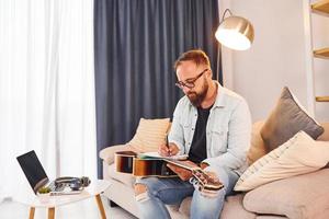 opvatting van creativiteit. Mens in gewoontjes kleren en met akoestisch gitaar is binnenshuis foto