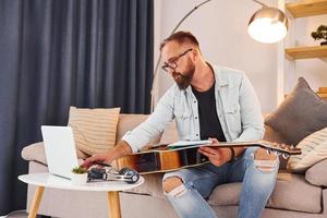 opvatting van creativiteit. Mens in gewoontjes kleren en met akoestisch gitaar is binnenshuis foto