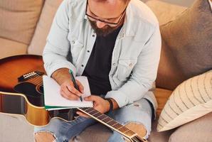 maken een liedje. Mens in gewoontjes kleren en met akoestisch gitaar is binnenshuis foto