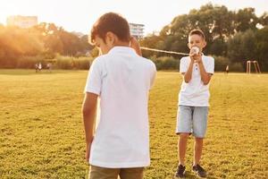 twee jongens hebben pret door gebruik makend van blik kan telefoon Aan de sportief veld- foto