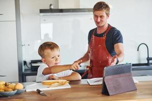 gebruik makend van tablet naar leren hoe naar koken. vader en zoon is binnenshuis Bij huis samen foto