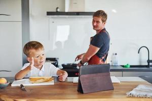 gebruik makend van tablet naar leren hoe naar koken. vader en zoon is binnenshuis Bij huis samen foto