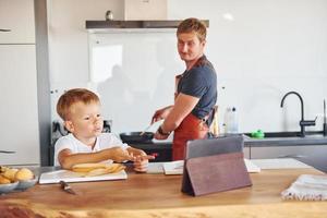 gebruik makend van tablet naar leren hoe naar koken. vader en zoon is binnenshuis Bij huis samen foto