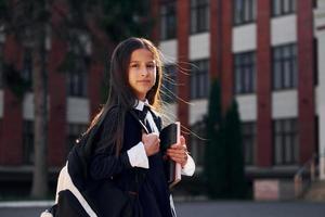 hebben een wandelen. schoolmeisje is buiten in de buurt school- gebouw foto