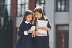 opvatting van onderwijs. twee schoolmeisjes is buiten samen in de buurt school- gebouw foto