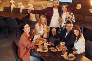 Holding bril. groep van jong vrienden zittend samen in bar met bier foto