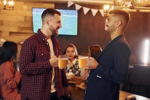 hebben een rust uit. groep van jong vrienden zittend samen in bar met bier foto